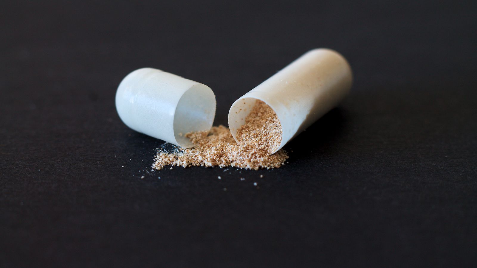 Close-up of a split capsule with powder spilling onto a dark surface.
